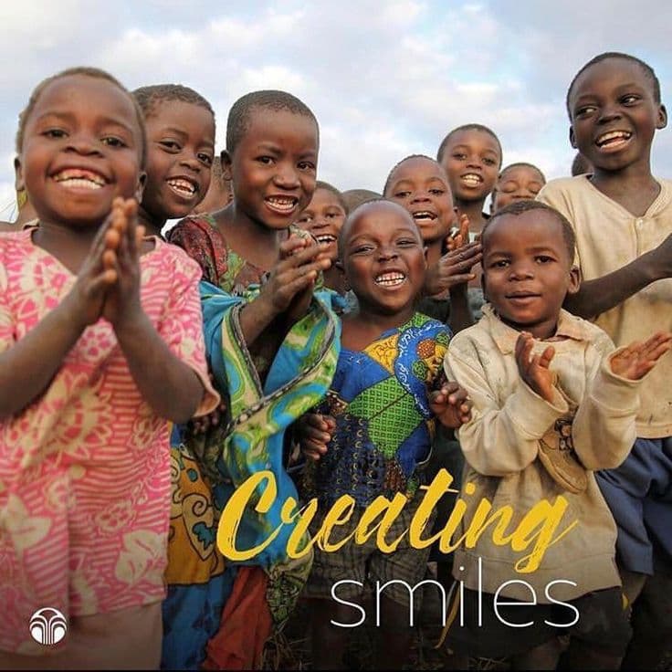 A group of joyful African children smiling and clapping, featuring the text 'Creating smiles' overlay.