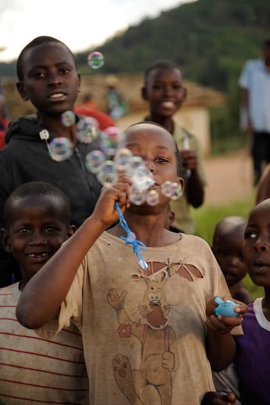 A young boy blowing bubbles, surrounded by other children in a rural village setting.