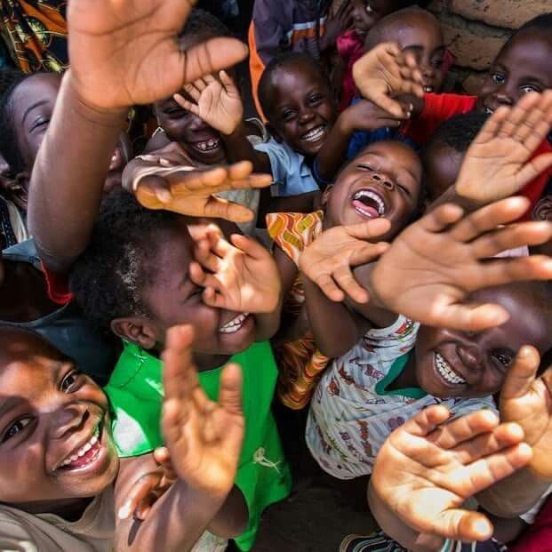 A group of joyful African children smiling and reaching their hands towards the camera lens.